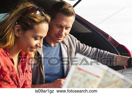 Stock Photo - Couple reading map behind vehicle. Fotosearch