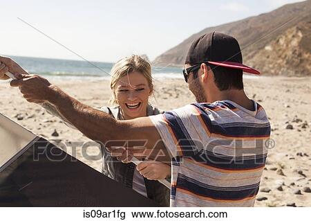 Stock Image - "Couple setting up tent on beach, Malibu, California, USA". Fotosearch
