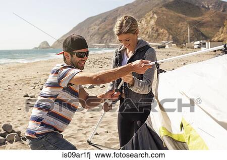 Stock Image - "Couple setting up tent on beach, Malibu, California, USA". Fotosearch