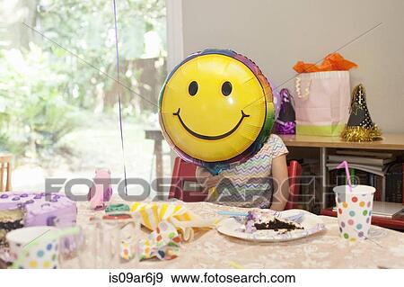 Girl sitting at birthday party table with cake playing with smiley face balloon View Large Photo Image Stock Photo - Girl sitting at birthday party table with cake playing with smiley face balloon. Fotosearch