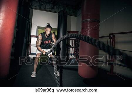 Stock Photography - Male boxer doing battle rope training in gym. Fotosearch