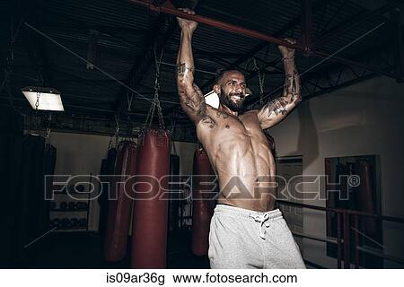 Stock Image - Male boxer doing pull ups with gritted teeth in gym. Fotosearch