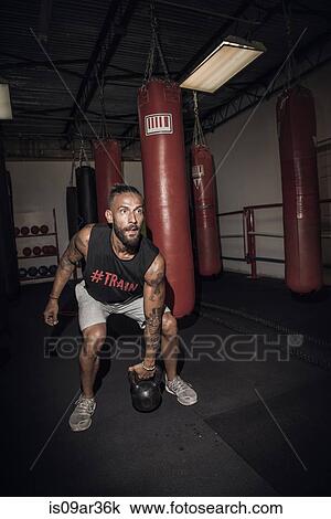 Stock Image - Male boxer preparing to lift kettlebell in gym. Fotosearch