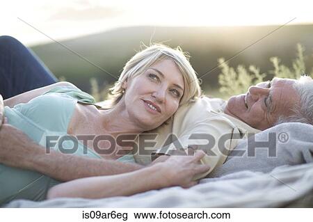 Stock Image - Mature couple lying together on blanket smiling. Fotosearch