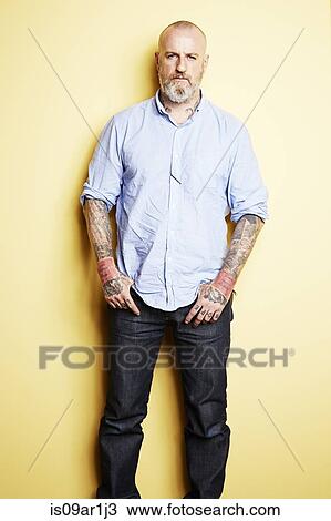 Stock Image - "Mature man with tattoos on arms and neck, yellow background". Fotosearch