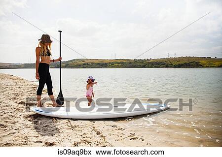 "Mid adult woman and toddler daughter with paddleboard on beach, Carlsbad, California, USA" View Large Photo Image Stock Photo - "Mid adult woman and toddler daughter with paddleboard on beach, Carlsbad, California, USA". Fotosearch