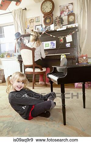 "Mother sitting at piano, whilst daughters play in room" View Large Photo Image Stock Photo - "Mother sitting at piano, whilst daughters play in room". Fotosearch
