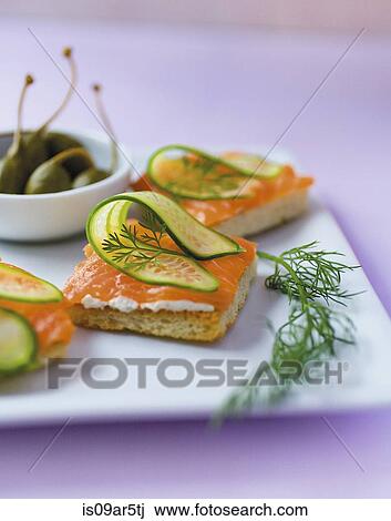 Stock Image - "Plate of crackers with sliced salmon, cucumber and dill". Fotosearch