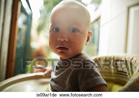 Stock Image - Portrait of baby boy looking at camera sitting in high chair. Fotosearch
