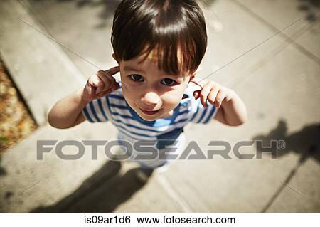 Stock Photograph - Portrait of boy putting his fingers in his ears on street. Fotosearch