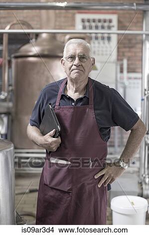 Picture - "Portrait of brewer in brewery, standing next to stainless steel tanks". Fotosearch