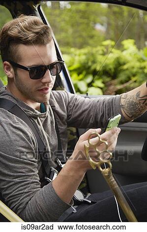 Stock Image - Portrait of man driving wearing sunglasses and using smart phone. Fotosearch