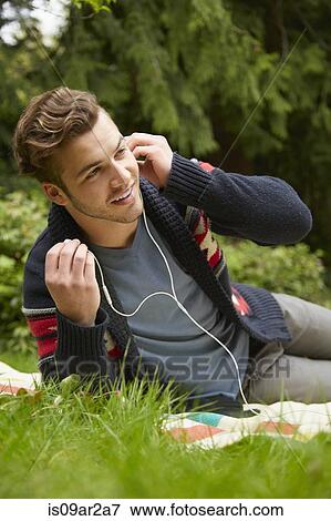 Stock Photo - Portrait of man laying in garden listening to smartphone wearing earphones. Fotosearch