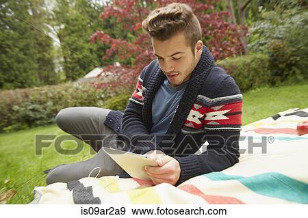 Stock Photo - Portrait of man laying in garden reading digital tablet. Fotosearch