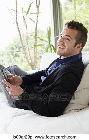 Portrait of man relaxing on sofa with feet up holding digital reading device View Large Photo Image Stock Photography - Portrait of man relaxing on sofa with feet up holding digital reading device. Fotosearch