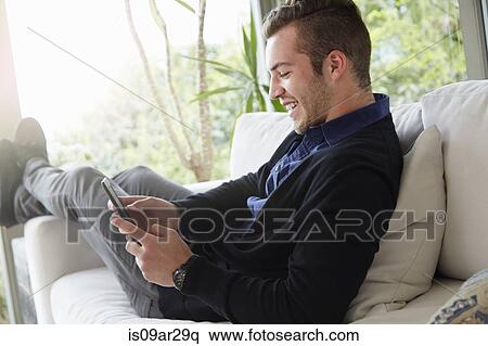 Stock Photography - Portrait of man relaxing on sofa with feet up looking at digital reading device. Fotosearch