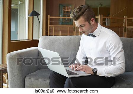 Stock Image - Portrait of man sitting on sofa working from laptop. Fotosearch
