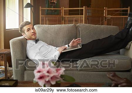 Stock Photo - Portrait of man wearing smart clothes laying on sofa using laptop. Fotosearch