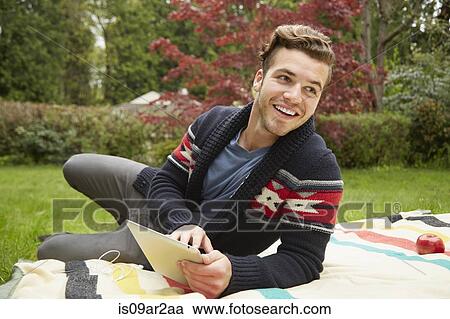 Portrait of smiling man laying in garden reading digital tablet View Large Photo Image Stock Image - Portrait of smiling man laying in garden reading digital tablet. Fotosearch