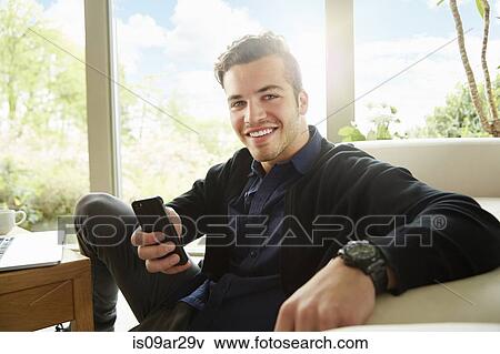 Stock Photo - Portrait of smiling man sitting on floor holding smartphone. Fotosearch