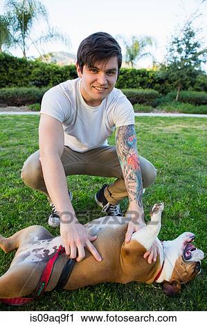 Stock Image - Portrait of young man in park playing with bulldog. Fotosearch