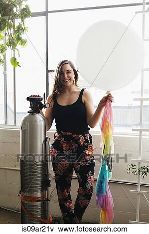 Portrait of young woman holding up helium balloon in design studio View Large Photo Image Stock Photo - Portrait of young woman holding up helium balloon in design studio. Fotosearch