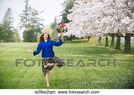 Picture - Portrait of young woman practicing yoga whilst holding bunch of flowers in park. Fotosearch