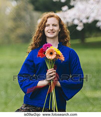 Portrait of young woman with long wavy red hair holding bunch of flowers in park View Large Photo Image Picture - Portrait of young woman with long wavy red hair holding bunch of flowers in park. Fotosearch