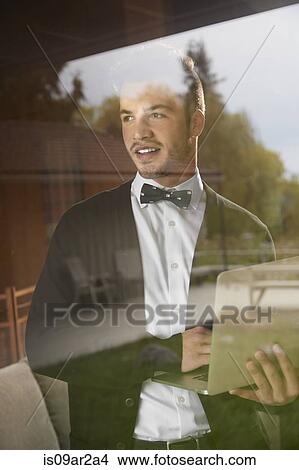 Shot through window of man standing looking out at the view holding laptop View Large Photo Image Picture - Shot through window of man standing looking out at the view holding laptop. Fotosearch