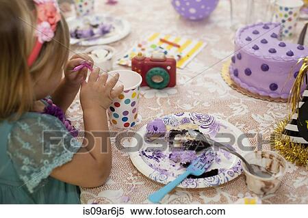Stock Photography - Side view of of girl sitting at birthday party table eating purple cake. Fotosearch