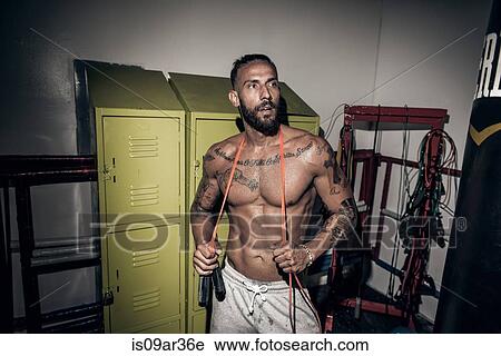 Stock Image - Tattooed male boxer with skipping rope in gym. Fotosearch
