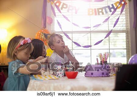 Stock Image - Three children sitting at table eating purple birthday cake. Fotosearch