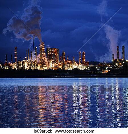 Stock Image - View of coastal oil refinery and smoke stacks at night. Fotosearch