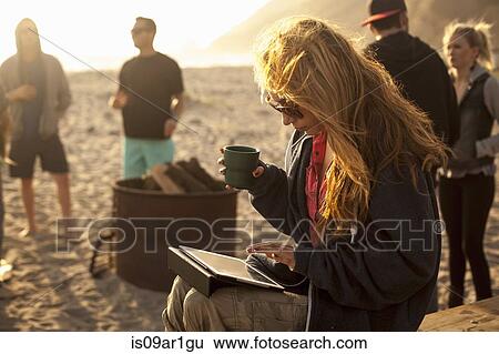 Stock Photograph - "Woman using digital tablet on beach, friends in background". Fotosearch