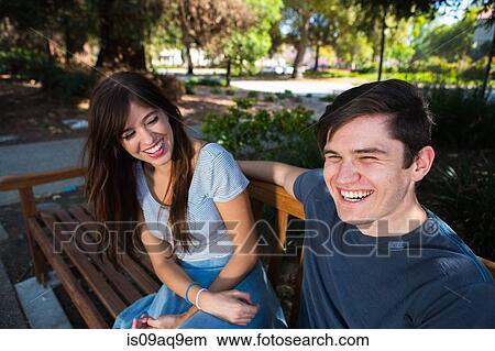 Picture - Young couple laughing on park bench. Fotosearch