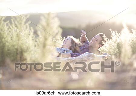 Stock Image - Young couple lying together outdoors laughing. Fotosearch