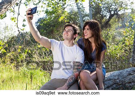 Young couple taking smartphone selfie in park View Large Photo Image Stock Photograph - Young couple taking smartphone selfie in park. Fotosearch