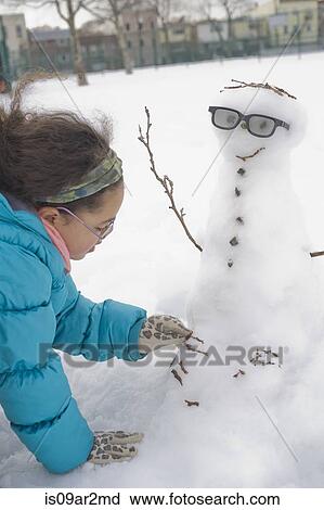 Stock Image - Young girl building snowman in snow. Fotosearch