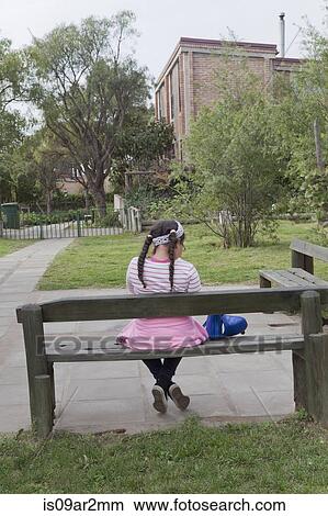 Picture - "Young girl sitting on bench, rear view". Fotosearch