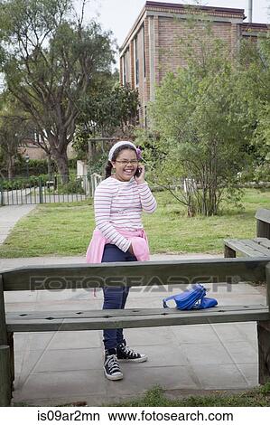 Young girl standing beside bench using mobile phone View Large Photo Image Picture - Young girl standing beside bench using mobile phone. Fotosearch