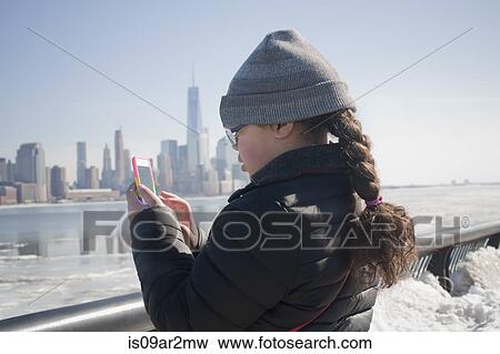 Stock Photo - "Young girl taking photograph of skyline using smartphone, New York, NY, USA". Fotosearch