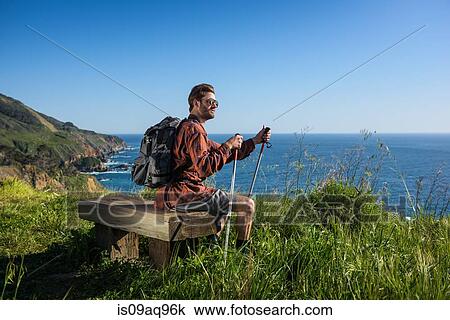 Young Male Hiker Looking Out From Cliff Top Bench Big Sur