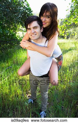 Stock Photograph - Young man giving girlfriend piggyback ride in park. Fotosearch