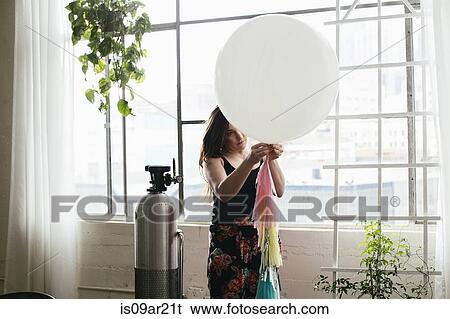 Stock Photograph - Young woman attaching bunting to balloon in design studio. Fotosearch