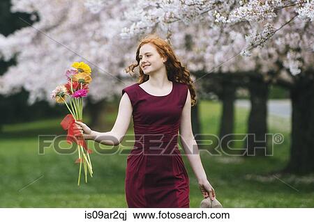 Stock Image - Young woman holding bunch of flowers in spring park. Fotosearch