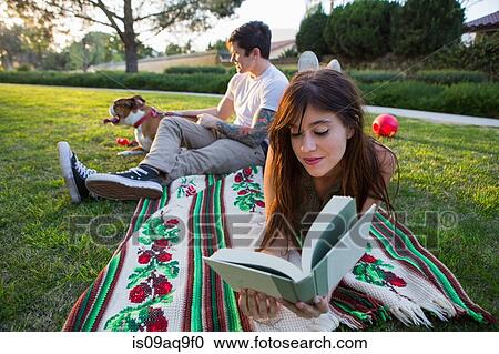 Young woman reading book whilst boyfriend pets dog in park View Large Photo Image Stock Image - Young woman reading book whilst boyfriend pets dog in park. Fotosearch