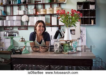 Stock Image - Bakery owner leaning over counter. Fotosearch