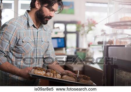 Stock Photography - Bakery owner placing tray of vegan, allergy-friendly doughnuts into display case. Fotosearch