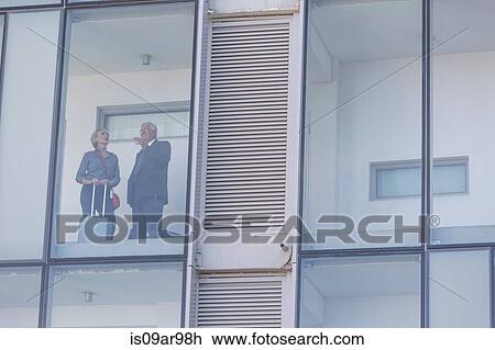 Stock Image - Businessman and woman talking in corridor of glass fronted hotel. Fotosearch