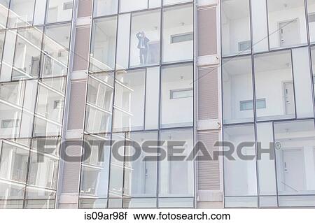 Businessman looking out of window of glass fronted hotel whilst talking on smartphone View Large Photo Image Stock Image - Businessman looking out of window of glass fronted hotel whilst talking on smartphone. Fotosearch